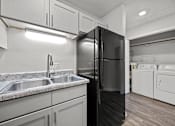 Thumbnail 27 of 52 - View of a black refrigerator in a kitchen with grey cabinets and view of the washer and dryer.
