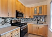 Thumbnail 20 of 51 - A kitchen with wooden cabinets and a black stove top oven at Brookmore Pasadena, CA apartments.