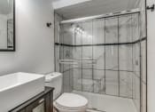 Thumbnail 6 of 43 - Fusion Fort Worth apartment renovated bathroom with veined marble tile, clear glass sliding door, and chrome trim on large shower.