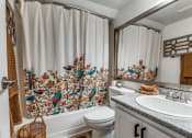 Thumbnail 19 of 43 - Renovated Bathroom in Fusion Fort Worth (previously Desert Sands) apartment in Haltom City. Teal, Red, and Camel colored birds embroidered on shower curtain in large bathtub.