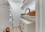 Thumbnail 5 of 43 - Fusion Fort Worth apartment walk in closet with wicker baskets on built in shelving, hangers on curtain rods, and white midcentury modern dresser.