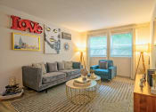 Thumbnail 2 of 25 - Living room at the Canvas Apartments, apt for rent in Nashville TN with large midcentury modern couch and sitting chair, large windows, and wood style flooring.