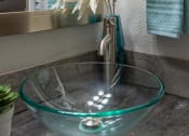 Thumbnail 14 of 49 - Bathroom sink in the Retreat at Indian Lake one bedroom apartment in Hendersonville with glass basin sink and chrome framed mirror.