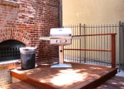 Thumbnail 17 of 29 - Brookmore Pasadena ca apartments grilling station with a stainless steel grill and trash can on a stained wood deck with railing and brick wall.