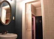 Thumbnail 14 of 29 - Bathroom in one bedroom brookmore apartment in Pasadena. Oval mirror over pedestal sink and doorway with white trim leads to hallway and front door.