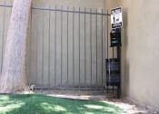 Thumbnail 23 of 29 - Pasadena Brookmore apartments dog run with artificial turf, a tall tree, and a pet waste disposal station with trash bags and trash can.