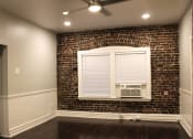 Thumbnail 9 of 29 - Living room in Brookmore apartments Pasadena CA. Large window with white blinds and trim and air conditioning unit on an exposed brick wall