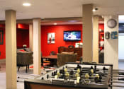 Thumbnail 19 of 29 - Brookmore apartments rec room with red walls. Features a football table and TV room with couches, console, and coffee table.