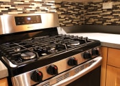 Thumbnail 10 of 29 - A six burner gas stove in a brookmore apartments kitchen with honey colored wood cabinets and multicolored backsplash.