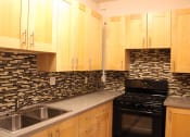 Thumbnail 12 of 29 - Kitchen in one bedroom brookmore apartment in Pasadena. Modern wood cabinets with silver pulls, multicolored tile backsplash, and black gas stove