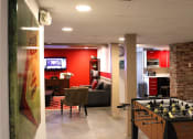 Thumbnail 18 of 29 - Brookmore apartments rec area with foosball table; kitchen area with toaster, microwave, and red cabinets; and living room with TV and couches.
