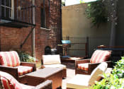 Thumbnail 16 of 29 - Brookmore Pasadena ca apartments back patio next to brick wall. Stained wood deck with cushioned wicker patio furniture and grill.