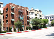 Thumbnail 27 of 29 - Street view of Brookmore apts in Pasadena CA. Four story brick building with striped awnings, fire escape, and "now leasing" sign.
