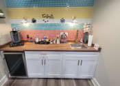 Thumbnail 54 of 60 - Fusion Orlando apartments coffee bar with butcher block counter, white cabinets, colorful tile wall, and Keurig with coffee pods and cups.