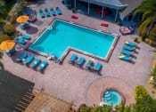 Thumbnail 40 of 60 - Community pool at Fusion Orlando Apartments aerial shot. Pool is surrounded by sixteen blue lounge chairs and patio tables with orange umbrellas.