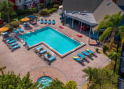 Thumbnail 38 of 60 - Aerial view of L-shaped community pool at furnished Fusion Apartments in Orlando, FL. Pool is surrounded by blue lounge chairs and palm trees.