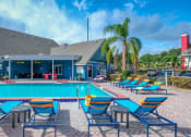 Thumbnail 36 of 60 - Fusion Orlando apartments community pool next to large pool house with covered patio, bright blue siding, and palm trees.