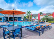 Thumbnail 35 of 60 - Fusion Orlando apartments community pool surrounded by blue patio lounge chairs and patio tables with bright orange umbrellas.
