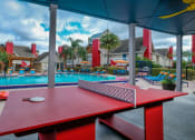Thumbnail 34 of 60 - Fusion Orlando apartments poolside activities including ping pong table, corn hole, and bright blue lounge chairs.
