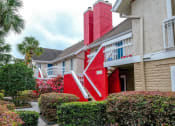 Thumbnail 48 of 60 - Two story Fusion Orlando apartments exteriors. Apartments have red staircases to second story and red chimneys, and tropical landscaping line paths.