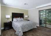 Thumbnail 16 of 60 - Fusion Orlando furnished studio apartment bedroom with sliding glass door to tropical patio with palm trees. Bed is large with grey duvet.