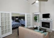 Thumbnail 11 of 60 - Fusion Orlando furnished apartment living room with built in fireplace, vaulted ceiling with modern fan, and tan couch with teal pillows.