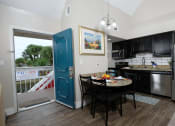 Thumbnail 8 of 60 - Fusion Orlando single bedroom apartment in Orlando second story apartment kitchen and dinette next to teal front door open to balcony with white railing.