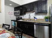 Thumbnail 6 of 60 - Fusion apartment for rent Orlando apartment kitchen with espresso cabinets, stainless steel appliances, and white tile backsplash.