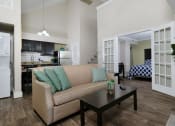 Thumbnail 5 of 60 - Fusion apartments complex Orlando, FL furnished apartment living room with tan couch with teal pillows, espresso coffee table, and glass French doors open to bedroom.