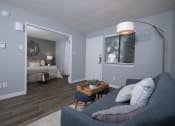 Thumbnail 10 of 43 - Fusion Fort Worth one bedroom apartment in Haltom City living area with wide door to bedroom furnished with large bed and modern blue couch.