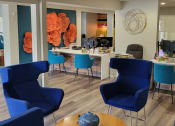 Thumbnail 51 of 60 - Fusion Orlando apartments entryway with desks with computers and waiting area with modern navy blue chairs around a wood coffee table.