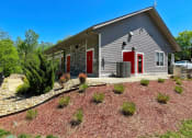Thumbnail 48 of 49 - Main office of The Retreat apts at Indian Lake in Hendersonville exterior with grey siding, red doors, and meticulous landscaping.