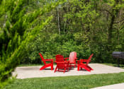 Thumbnail 45 of 49 - The Retreat apartments at Indian Lake in Hendersonville outdoor seating area with four red Adirondack chairs and barbecue on concrete slab.