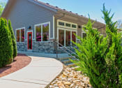 Thumbnail 44 of 49 - The Retreat apts at Indian Lake in Hendersonville community building exterior with grey siding, river rock wainscoting, and white trim windows.