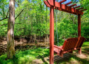 Thumbnail 43 of 49 - The Retreat at Indian Lake in Hendersonville apartment grounds with stained wooden bench swing overlooking creek.