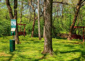 Thumbnail 42 of 49 - Dog area at The Retreat at Indian Lake in Hendersonville with pet waste station and wooden bench swings amidst tall trees in green grass.