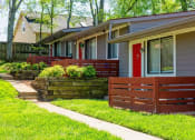 Thumbnail 41 of 49 - Row of apts at The Retreat at Indian Lake in Hendersonville with red front doors, grey siding, and green landscaping.