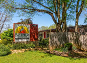 Thumbnail 37 of 49 - The Retreat apts at Indian Lake  monument sign in river rock planter with green landscaped bushes and shaded by tall trees.
