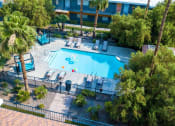 Thumbnail 13 of 23 - Aerial view of Fifteen 50 Apartments in Las Vegas with pool with blue cabanas, lounge chairs, and palm tree desert landscaping.