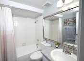 Thumbnail 15 of 43 - Fusion Fort Worth studio apartments Fort Worth. Bathroom with white tile tub and ombre shower curtain, white toilet, and single sink with vanity light and mirror.