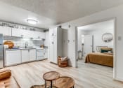 Thumbnail 2 of 43 - Fusion Fort Worth Apartments renovated kitchen area in Haltom City, TX with light wood plank flooring and subway tile backsplash, white appliances, and large bedroom door.