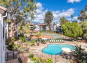 Thumbnail 15 of 15 - Fusion Warner Center apartments pool surrounded by black iron safety fencing next to tennis courts and courtyard with cabanas and lounge chairs.