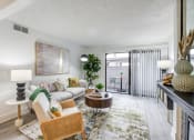 Thumbnail 3 of 15 - Fusion Warner Center luxury apartments for rent Woodland Hills living room with modern grey couch, abstract green and blue rug, and rattan rocking chair with cream cushion.
