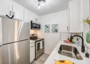 Thumbnail 4 of 15 - Woodland Hills apt for rent. Fusion Warner Center luxury apartment galley kitchen with stainless steel appliances, white cabinets, and white tile backsplash.