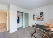 Thumbnail 6 of 15 - Fusion Warner Center luxury two bedroom apartment in Woodland Hills carpeted office with minimalist desk, closet, and modern painting on wall.