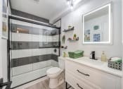 Thumbnail 7 of 15 - Fusion Warner Center apartments In Woodland Hills, CA bathroom with black and white tiled shower, lit mirror, and vanity sink with drawer storage.