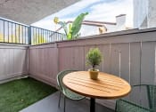 Thumbnail 9 of 15 - Fusion Warner Center luxury apartments in Woodland Hills bottom floor patio with tall wooden fence, patch of lush grass, and modern patio table and chairs.