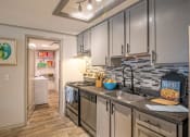 Thumbnail 4 of 49 - Kitchen in the Retreat apts at Indian Lake in Hendersonville with grey tile backsplash and door into large pantry with in-unit laundry.