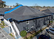 Thumbnail 30 of 38 - A grya building with a blue roof is surrounded by a parking lot at Mandarin Bay Apartments on San Jose Blvd
