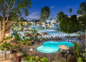 Thumbnail 13 of 15 - Fusion Warner Center luxury apartments in Woodland Hills pool, courtyard, and tennis courts lit at night and surrounded by palm trees.
